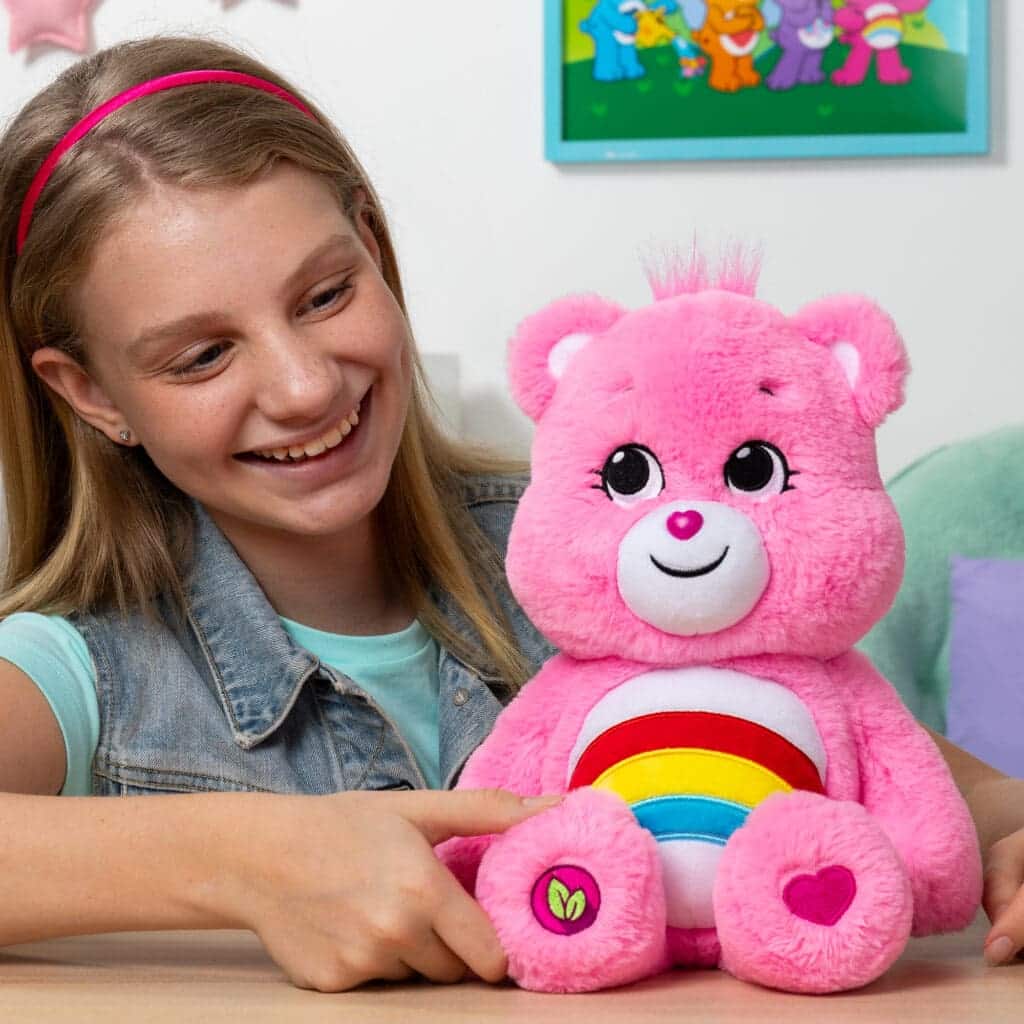 Care Bears Cheer plush displayed in a lifestyle setting with a young girl smiling.