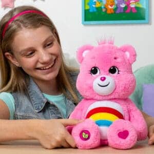 Care Bears Cheer plush displayed in a lifestyle setting with a young girl smiling.