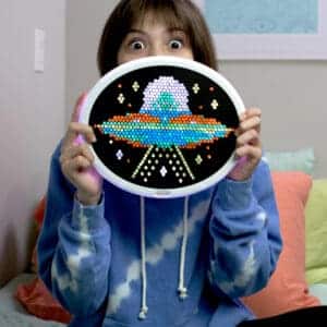 Girl excitedly holding Lite Brite Oval HD Grid with a spaceship displayed on it.