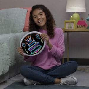Young girl sitting on the floor holding Oval HD Lite Brite with birthday cake displayed.