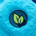 Close-up of a blue Grumpy Bear plush toy from the Care Bears collection, highlighting its embroidered rain cloud with raindrops and hearts on its belly. The toy has a slightly frowning expression and detailed stitching.