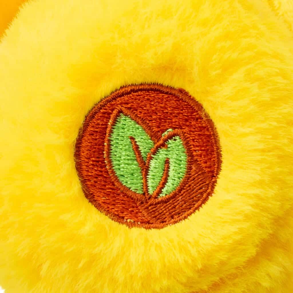 Close-up of a yellow Funshine Bear plush toy from the Care Bears collection, focusing on its embroidered emblem on its foot. The toy features detailed stitching and a soft, textured surface.