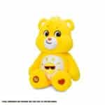 A yellow Funshine Bear plush toy from the Care Bears collection is shown against a plain white background. The toy features a smiling sun on its belly and has a cheerful expression.