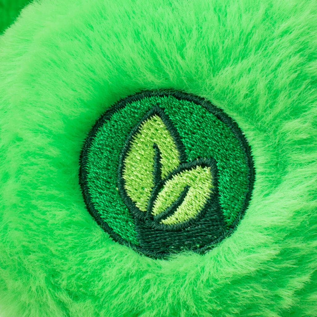 Close-up of a green Good Luck Bear plush toy from the Care Bears collection, showing embroidery on the bottom of bear's foot.