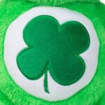 Close-up of a green Good Luck Bear plush toy from the Care Bears collection, highlighting its embroidered four-leaf clover on its belly.
