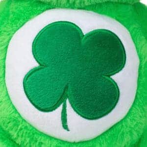 Close-up of a green Good Luck Bear plush toy from the Care Bears collection, highlighting its embroidered four-leaf clover on its belly.