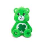 A green Good Luck Bear plush toy from the Care Bears collection is shown against a plain white background. The toy features a four-leaf clover on its belly and a cheerful expression.