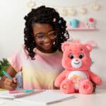 Love-A-Lot Bear on table with young girl smiling.
