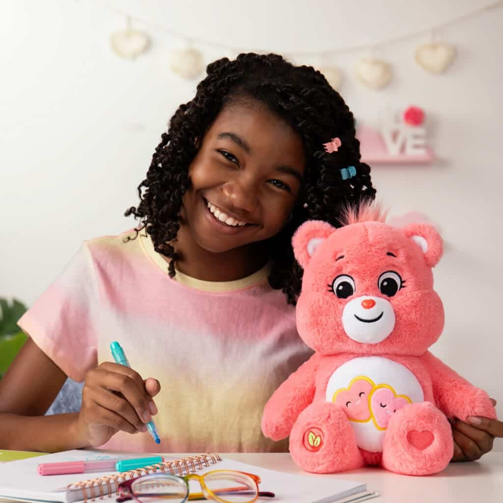 Love-A-Lot Bear on table with young girl smiling.