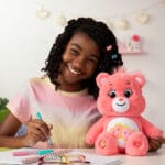 Love-A-Lot Bear on table with young girl smiling.