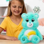 Light Blue Wish Bear on table with young girl smiling.