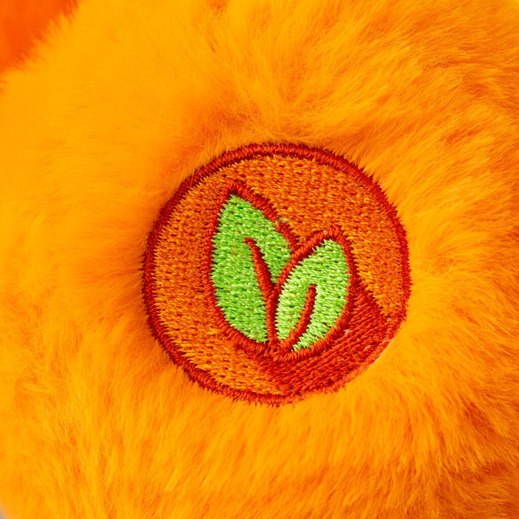 Close-up of an orange Friend Bear plush toy from the Care Bears collection, highlighting its embroidered foot.