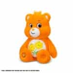 An orange Friend Bear plush toy from the Care Bears collection is shown against a plain white background. The toy features two intertwined smiling flowers on its belly and has a cheerful expression.