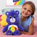 Violet Harmony Bear on bed with young girl smiling.