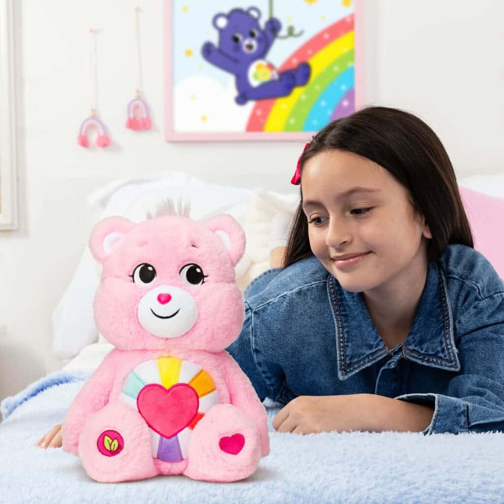 Pink Hopeful Heart Bear on bed with young girl looking.