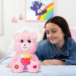 Pink Hopeful Heart Bear on bed with young girl looking.
