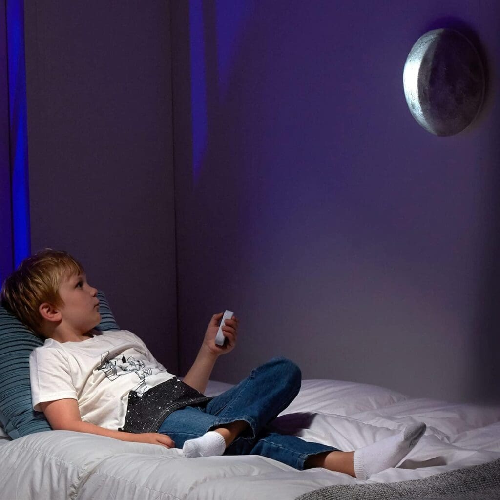Young boy shining Uncle Milton In My Room on wall while laying in bed.
