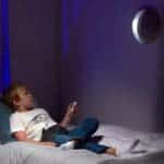 Young boy shining Uncle Milton In My Room on wall while laying in bed.