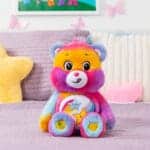 A Dare to Care Bear plush toy from the Care Bears collection is placed on a bed.