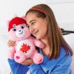 Young girl hugging Care Bear True North Bear on table.