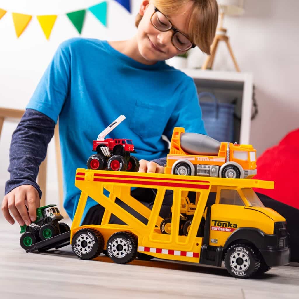 Young boy playing with Tonka Steel Classics Classic Car Carrier in bedroom.