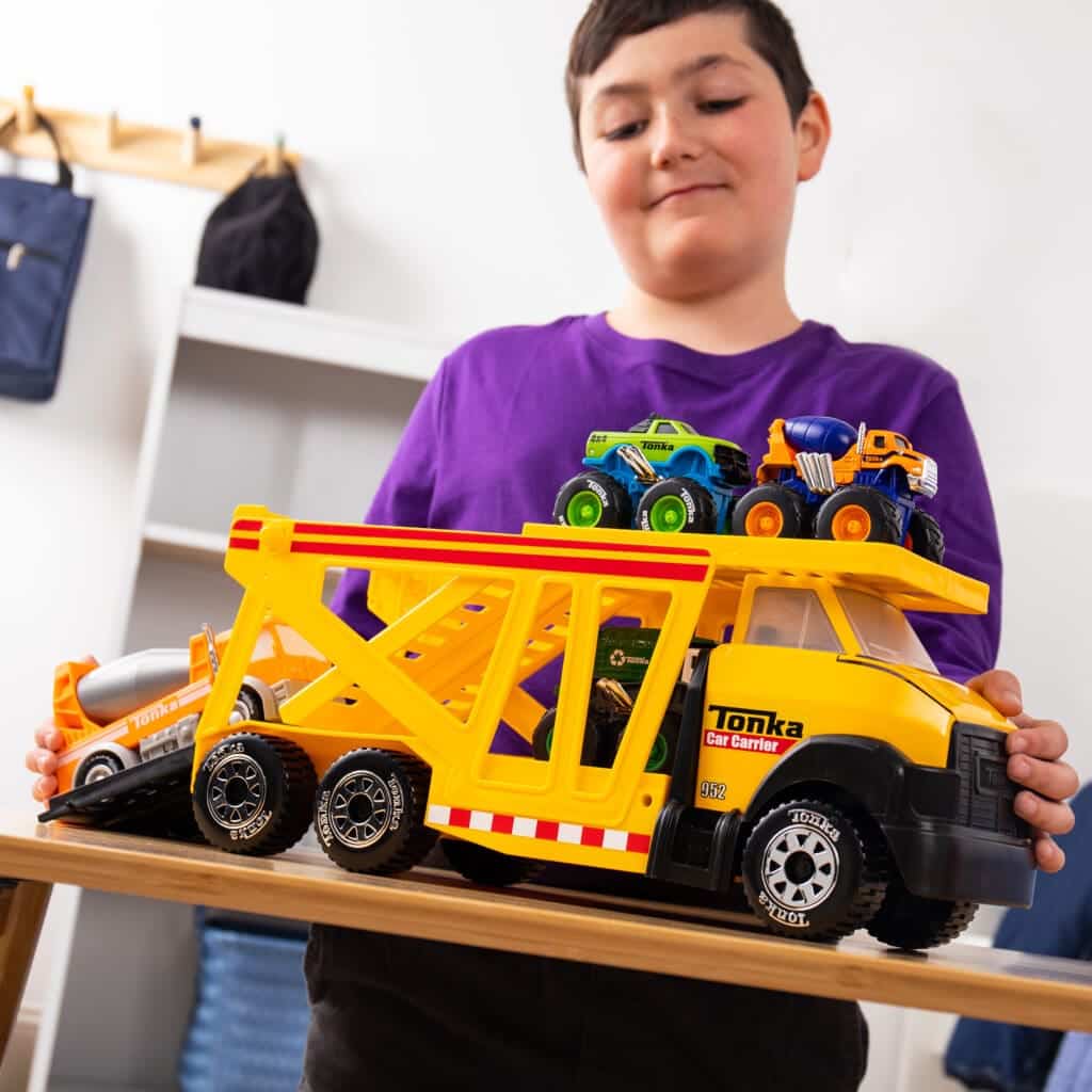 Young boy playing with Tonka Steel Classics Classic Car Carrier in bedroom.