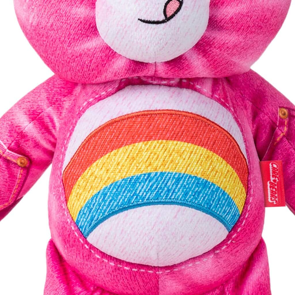 Close up of Care Bears Denim Share Bear, highlighting rainbow stomach emblem against white background.