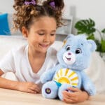 Young girl looking at Care Bears Medium Plush Sea Freind Bear with sun stomach emblem.