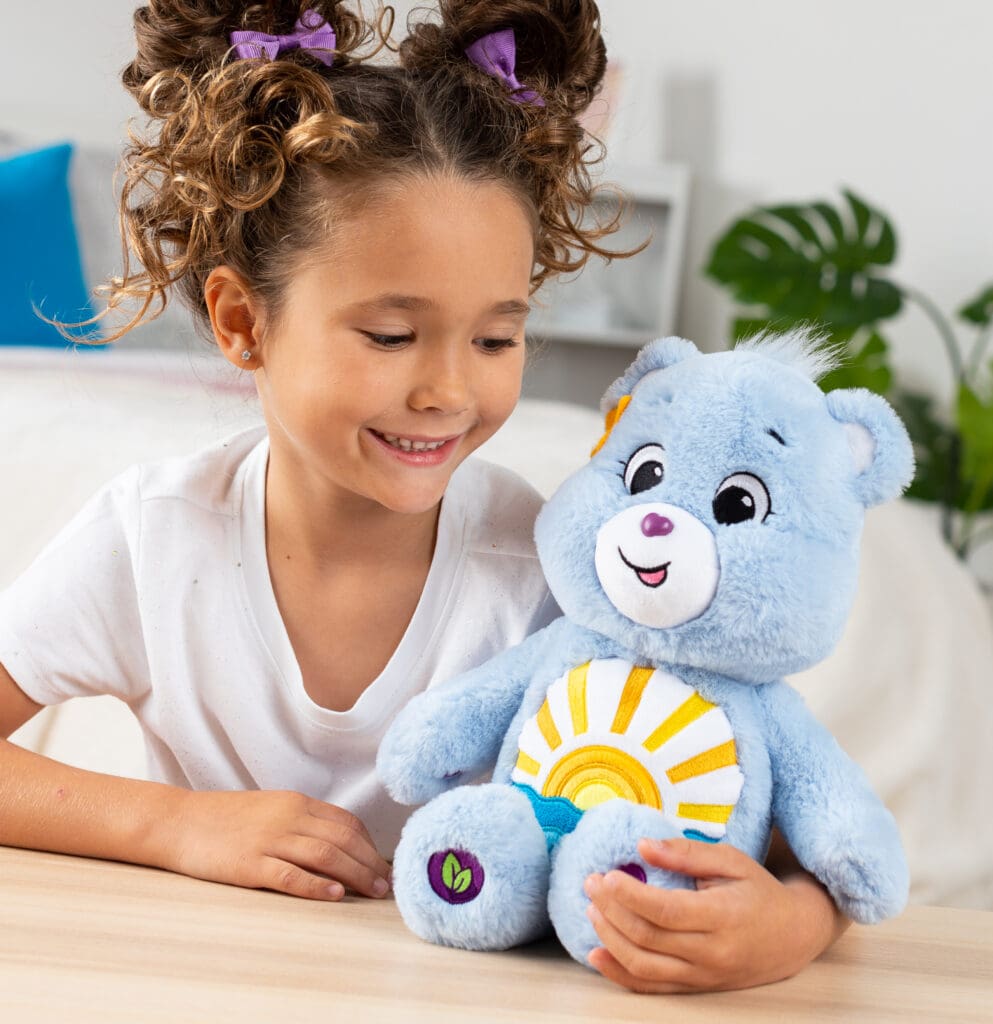 Young girl looking at Care Bears Medium Plush Sea Freind Bear with sun stomach emblem.