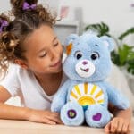 Young girl looking at Care Bears Medium Plush Sea Freind Bear with sun stomach emblem.
