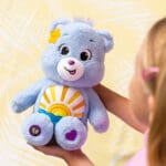 Young girl holding Care Bears Medium Plush Sea Freind Bear with sun stomach emblem.