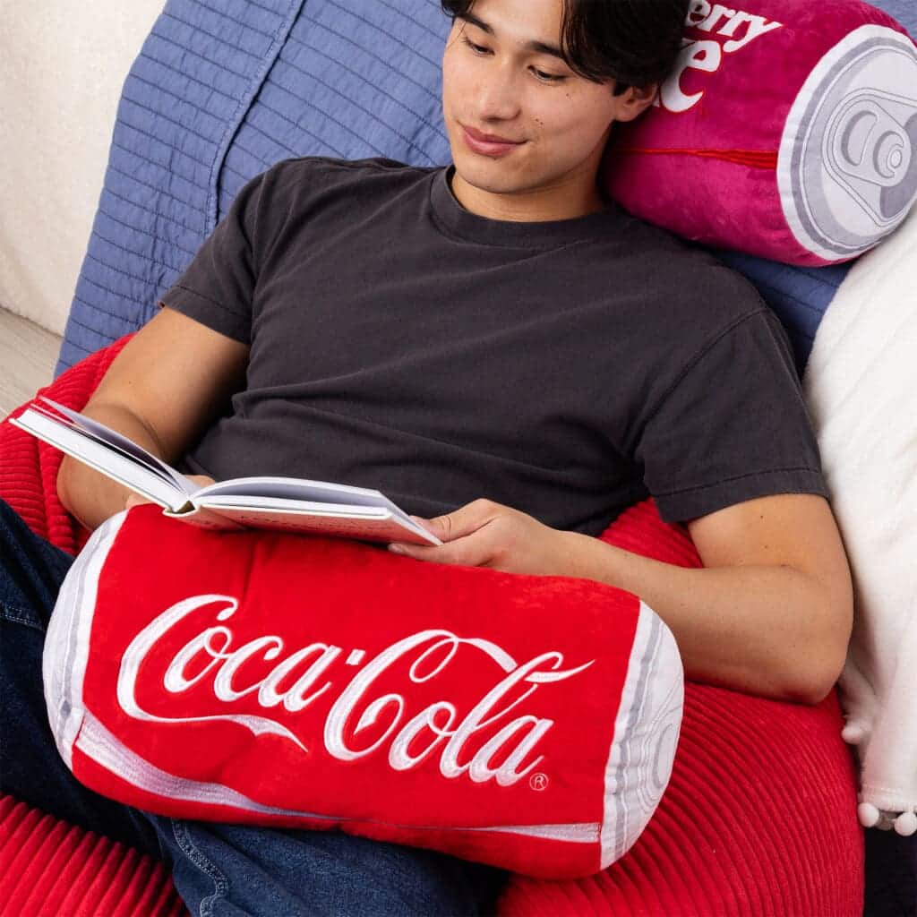 Young boy reading a book with Coca-Cola Novelty Plush Can on his lap.
