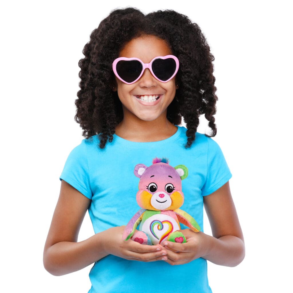 Young girl wearing sunglasses is holding Care Bear Fun Sized Togetherness Bear.