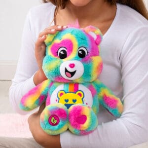 A colorful Good Vibes Bear plush toy from the Care Bears collection is being held by a young girl.