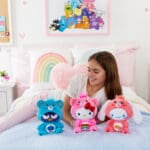 Three Care Bears Funsize plush with a young girl displayed in a lifestyle setting, surrounded by colorful decorations, promoting a playful and cheerful atmosphere.