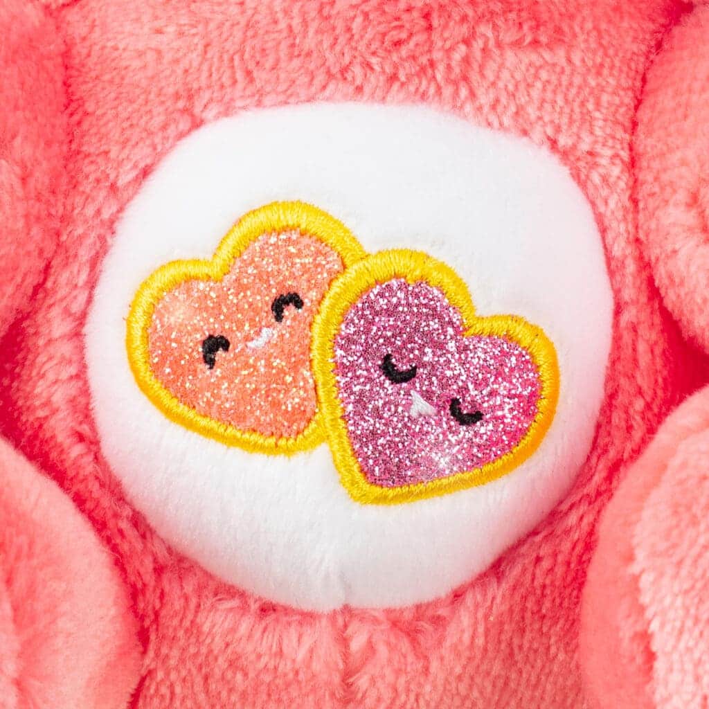 Close-up of the Care Bears Funsize Cinnamoroll plush, showcasing the pink heart emblem on its stomach, against a white background.