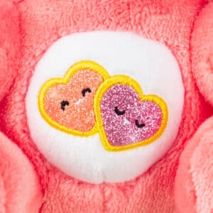 Close-up of the Care Bears Funsize Cinnamoroll plush, showcasing the pink heart emblem on its stomach, against a white background.