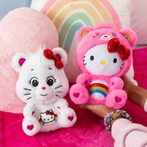 Care Bears Hello Kitty 2 Pack being held by a child's hand on her bed with pillows behind.