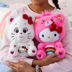 Care Bears Hello Kitty white and pink plush toys with rainbows on their stomachs, held by a child's hand.