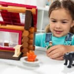 Close up of little girl playing with the boy figurine outside of the Lincoln Logs Adventure Pod Cabin