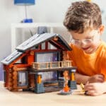 Child playing with the toy man figurine in front of the fully built Lincoln Logs Beechwood Retreat