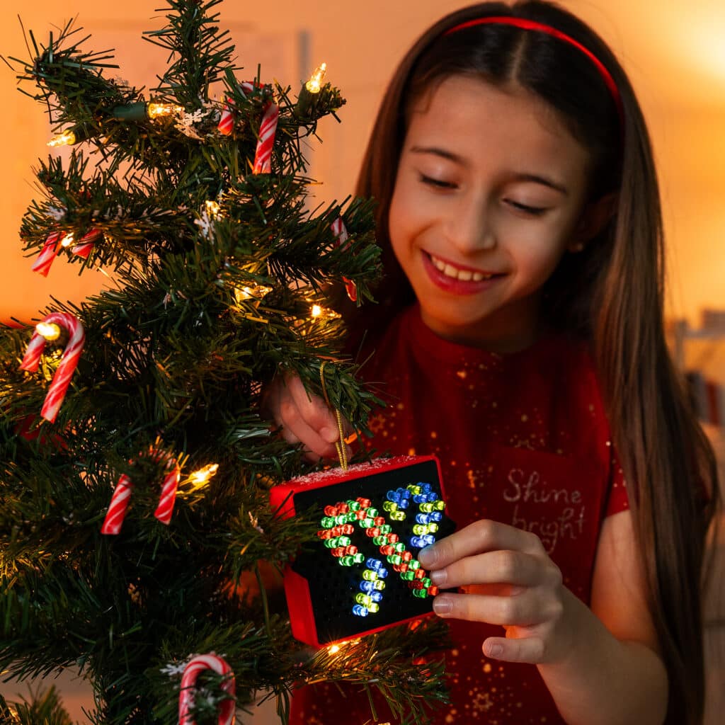 Little girl hanging the Lite-Brite Mini, Holiday Edition on to a Chirstmas tree