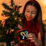 Little girl hanging the Lite-Brite Mini, Holiday Edition on to a Chirstmas tree