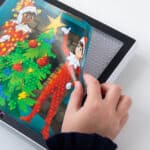 Photo shows someone applying a new background for the Lite Brite in continue playing and designing. Lite-Brite ColorPOP! Elf on the Shelf