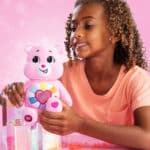 Little girl playing with the Care Bears Hopeful Heart Bear from the Sparkle Fun Sized collection