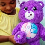 Little girl holding Cozy Share Bear looking at the eco friendly badge on its foot