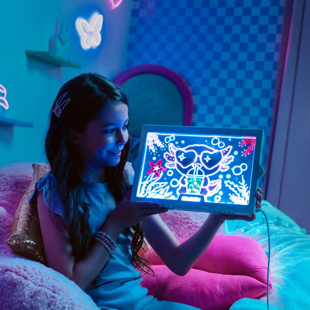 Girl in a neon-lit bedroom holding a glowing Lite-Brite Glowboard with traced and dotted art